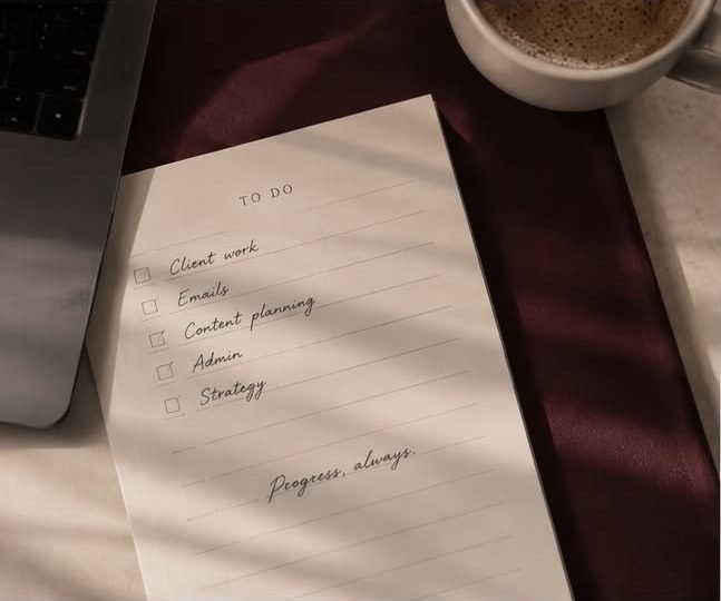 Handwritten to-do list — client work, emails, content planning, admin, strategy — next to a coffee and laptop
