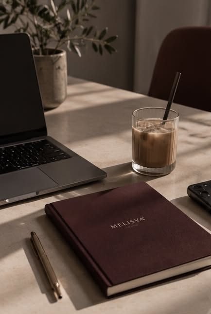 Laptop, iced coffee and a Melisva notebook on a sunlit desk